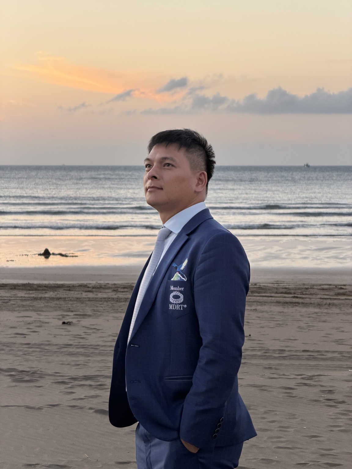 楊鈞緯穿著深藍西裝,站在夕陽下的海邊